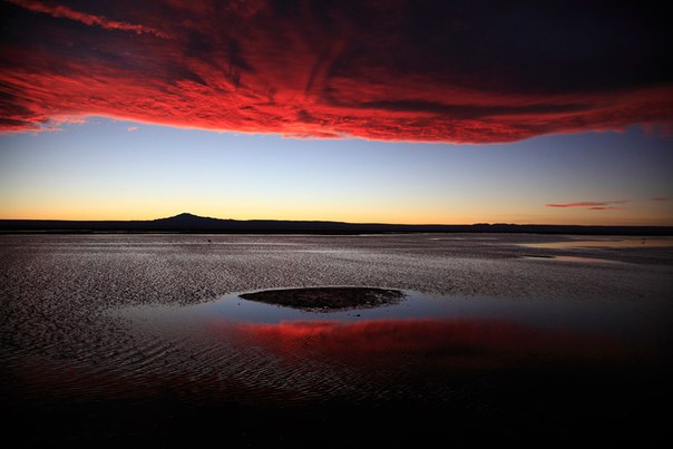 Лучи заходящего солнца освещают облака над солончаком Салар-де-Атакама на севере Чили.