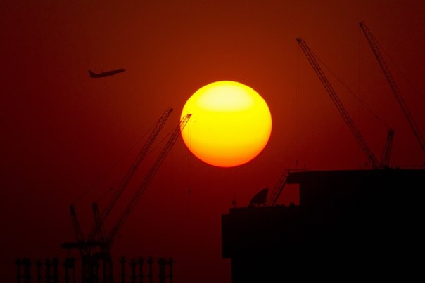 Пассажирский самолёт летит на фоне заходящего солнца в Шанхае.