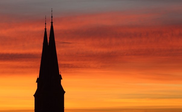 Шпили церкви Familienkirche виднеются на фоне рассветного неба в Вене.