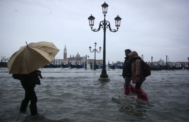 Люди идут по затопленной улице во время наводнения в Венеции.