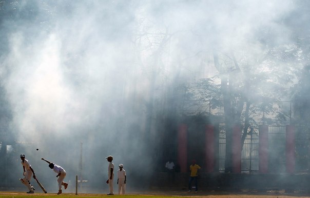 Индийские дети играют в крикет, в то время как муниципальные работники распыляют дезинфицирующее средство в связи с учащением случаев заболевания малярией в Мумбаи, Индия