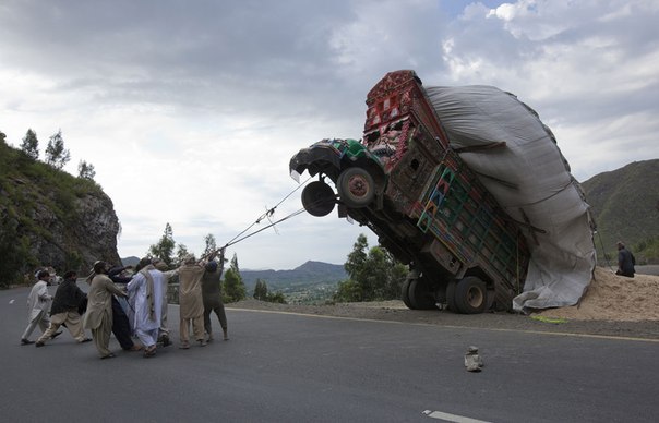 Люди пытаются выровнять грузовик, перегруженный пшеничной соломой, которая используется в качестве корма для скота, Даргай, район Малаканд, к северо-западу от столицы Пакистана Исламабада.