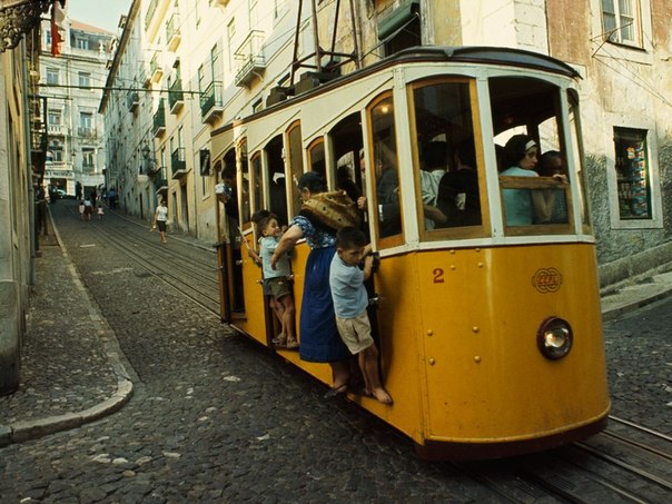Забитый до отказа трамвайчик с шумом едет по мощеным улочкам, везя лиссабонцев из Баирро Альто, в 1965 году. Небольшие трамвайчики работают по сей день, проезжая по узким улочкам мимо рынков, ресторанов и церквей. 