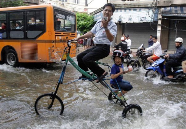 Таиландец едет с сыном на самодельном трехколесном велосипеде, предназначенном для передвижения во время наводнения.