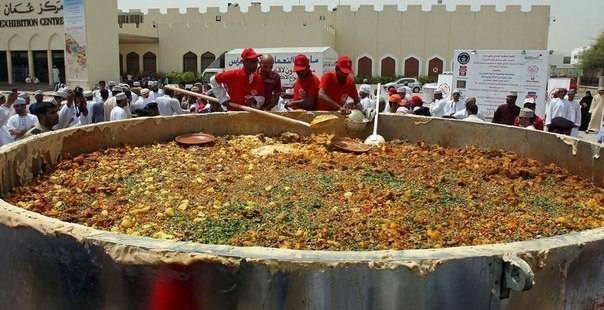 Оманцы мешают ингредиенты в огромном котле. Они готовят традиционною блюдо «кабса».