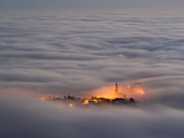 Плато Асьяго, Италия. Небольшой город, стоящий на холме, окутан туманом. 