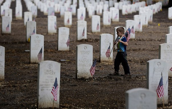 Мальчик помогает расставлять флажки на мемориальном кладбище Форт Сэм Хьюстон накануне празднования Дня памяти в Сан-Антонио, штат Техас
