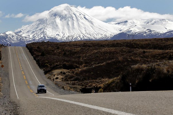 Автомобиль едет по национальной автостраде № 1 на фоне заснеженных вершин в национальном парке Тонгариро в Новой Зеландии.
