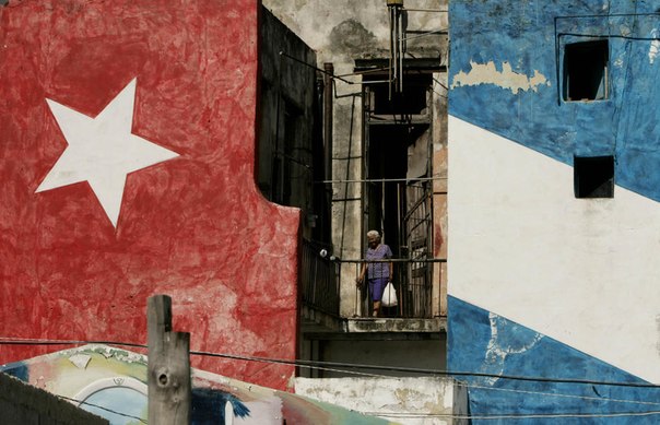 Женщина стоит на балконе возле стены, раскрашенной в цвета кубинского флага, в Гаване.