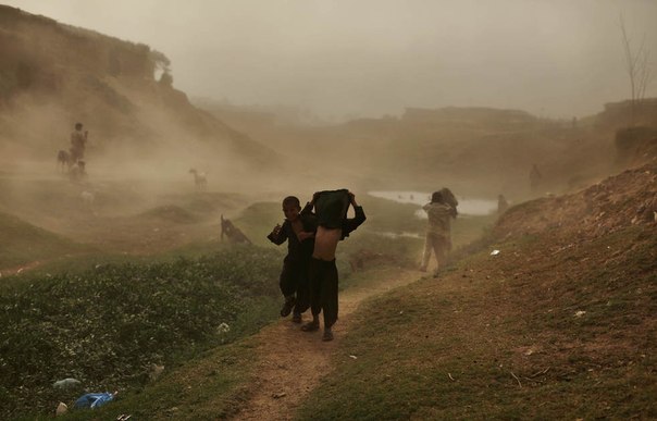 Дети афганских беженцев идут по району трущоб во время песчаной бури на окраине Исламабада, Пакистан.