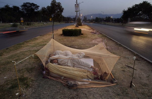 Автомобили проезжают мимо пакистанцев, которые спят под сеткой от комаров, на улице в Исламабаде, Пакистан.