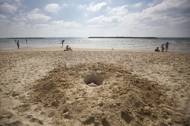 Израильтянин копает яму в песке на пляже в Тель-Авиве, Израиль.
