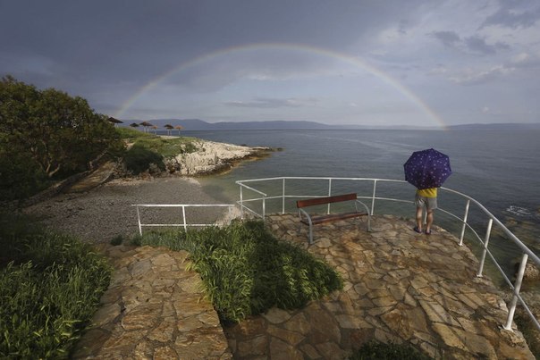 Мужчина любуется радугой над хорватским островом Црес в Адриатическом море.