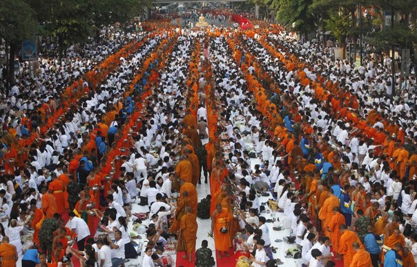 Буддийские монахи проходят мимо людей во время церемонии массового подаяния в Бангкоке.