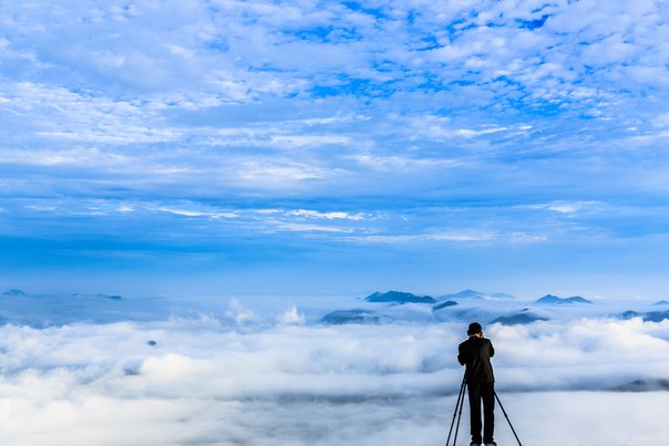 Мужчина фотографирует облака над городом с горы Yangbaeksan, Южная Корея.