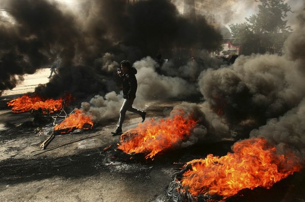 Студент-демонстрант проходит мимо горящих шин во время акции протеста против повышения цен на топливо возле автозаправочной станции в Макассаре, Индонезия.